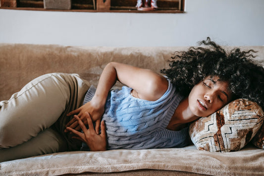 A woman laying down on a brown couch with cramps